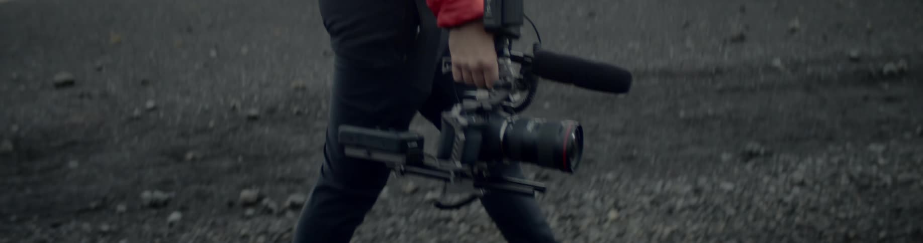 Man carrying a camera walks on the black sand on a cloudy day