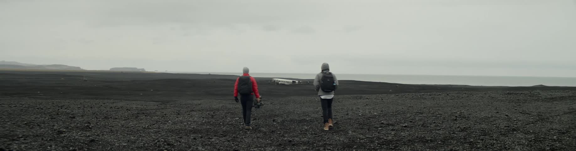 Two men walk on the black sand towards solheimasandur plane wreck