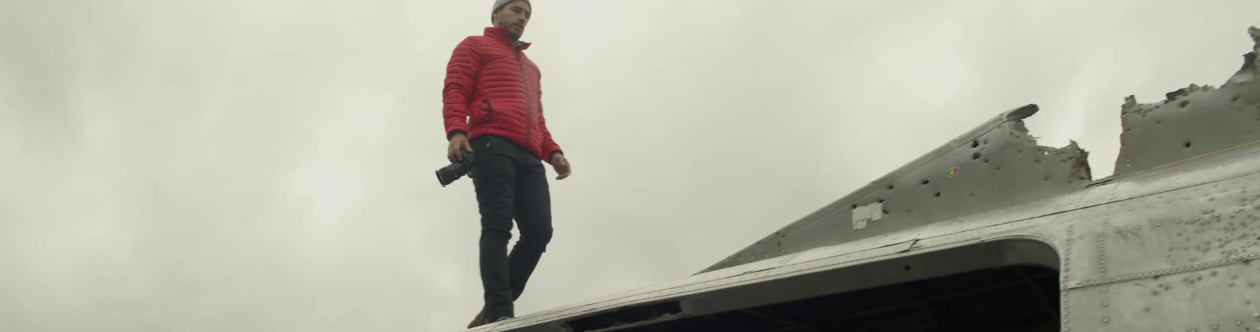 A man holding a camera stands on a damaged metal structure