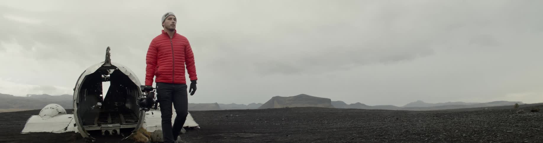 Man holding a camera walking out of old plane wreckage in the middle of a field