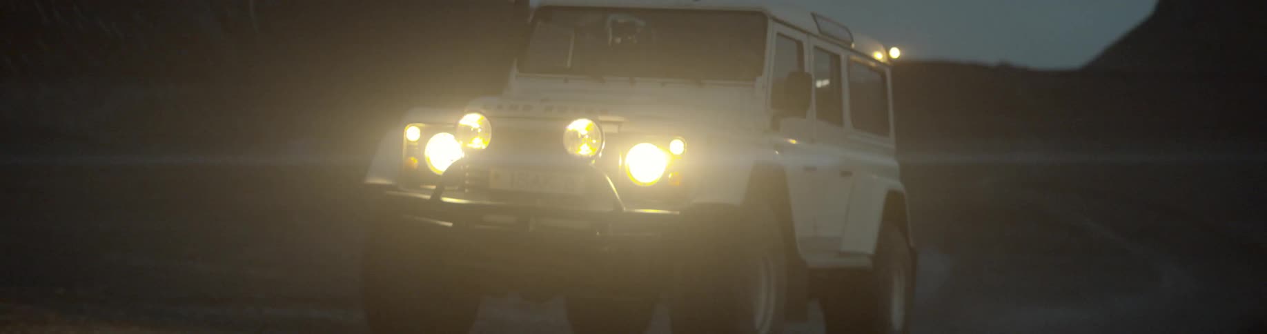 Jeep drives along dirt road near mountains at night