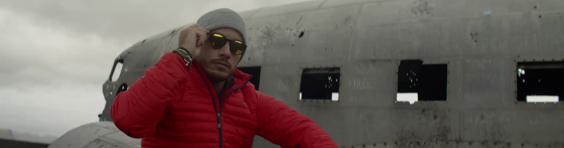 Man wearing red coat sits on wing of junked airplane