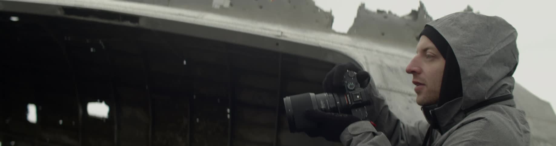 A man wearing a heavy jacket holds a camera up as he prepares to take a photograph