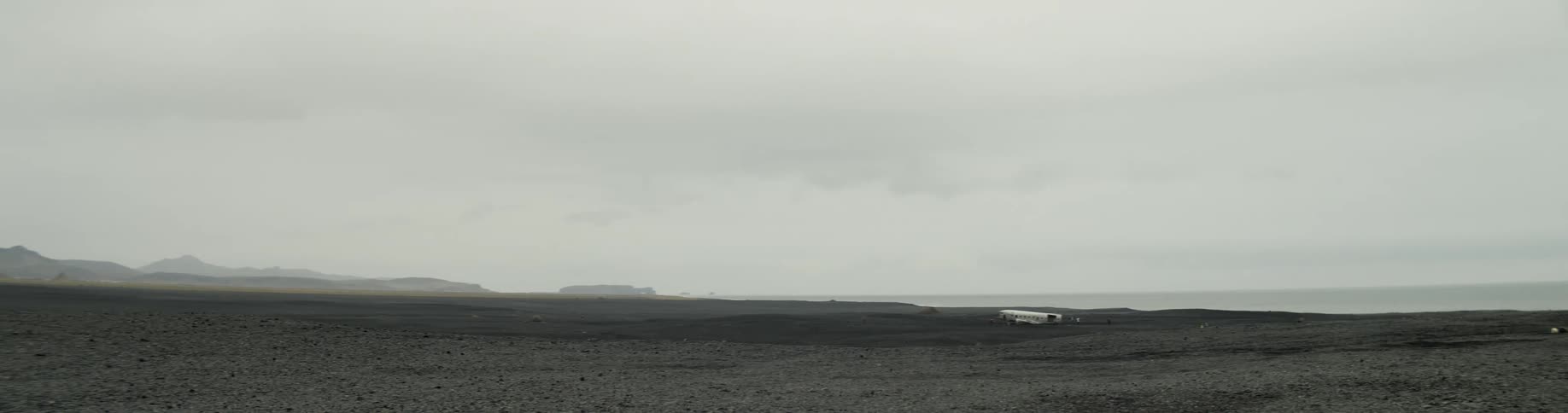 The fuselage of a wrecked plane on black sand on a cloudy day