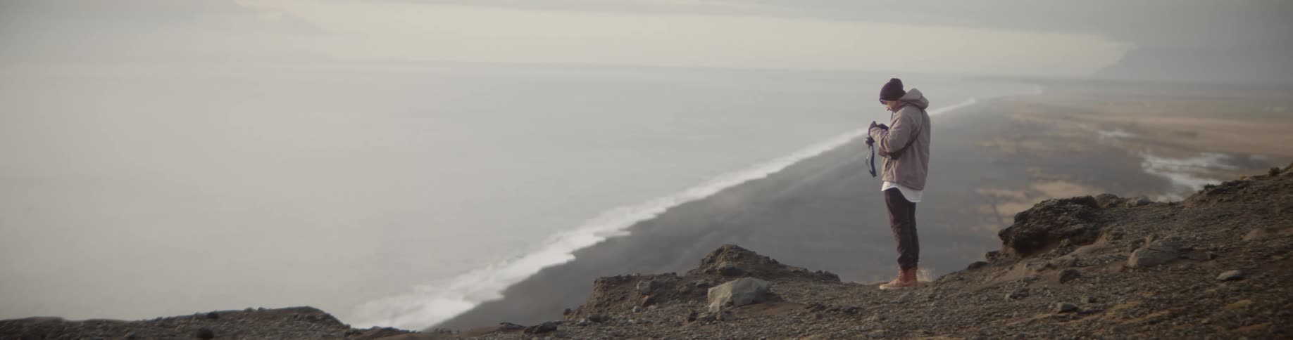 Man standing on the edge of the cliff takes a picture of the seashore