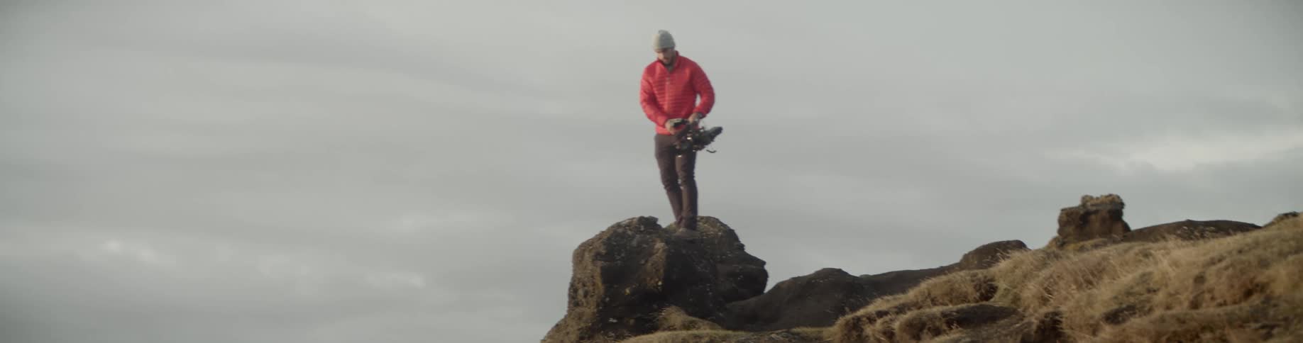 Man standing on a big rock at the edge of a cliff holds a camera
