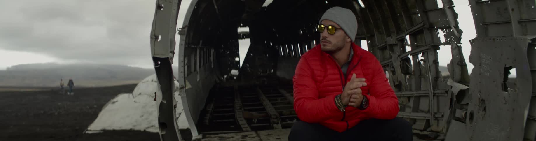 Man sitting in the ruined shell of an airplane looking out at the surroundings