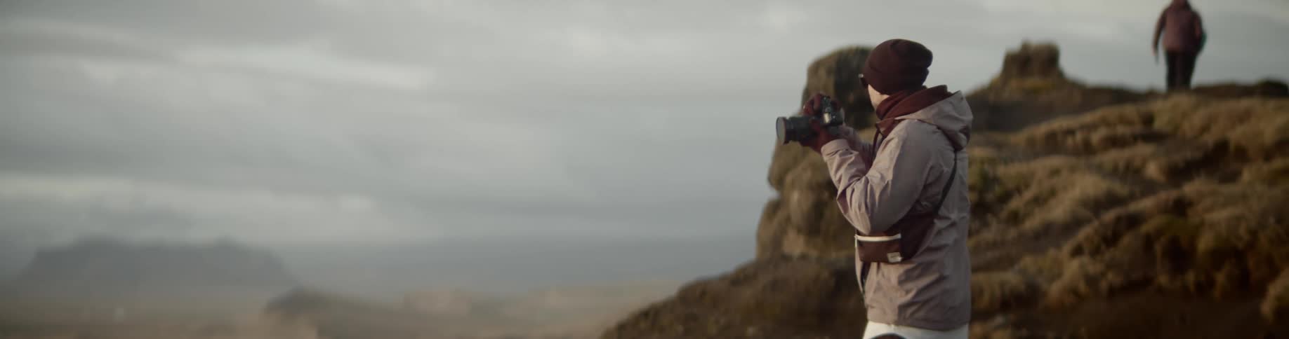 Photographer standing on cliff takes photo of landscape
