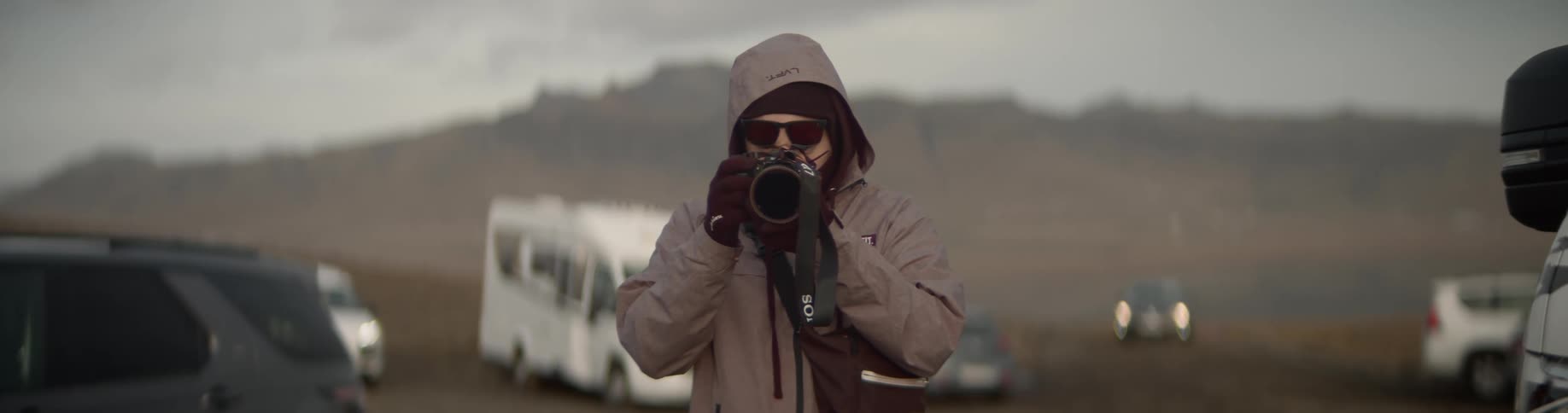 A man wearing a hooded jacket holds up a camera as he prepares to take a photo