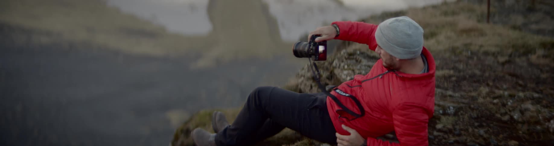 A white male sits on the edge of a cliff and takes photos