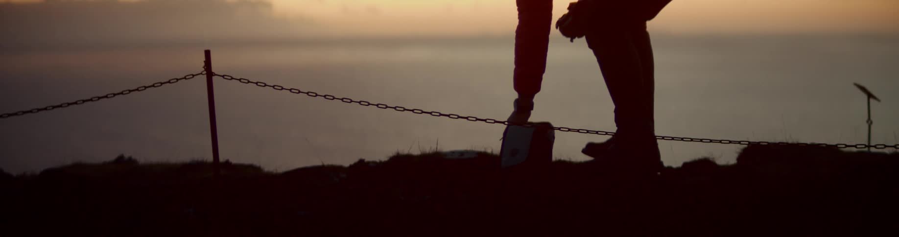 A man leans over on the cliff to reach in a bag