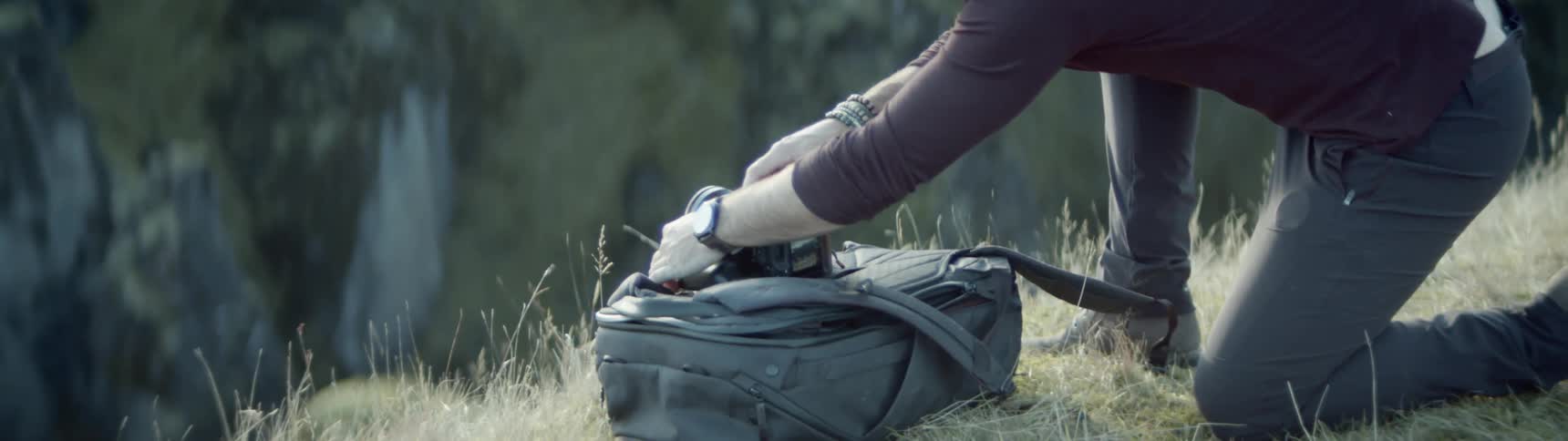 A man kneels on the grass as he sets up a camera on a backpack to take a photo of nature