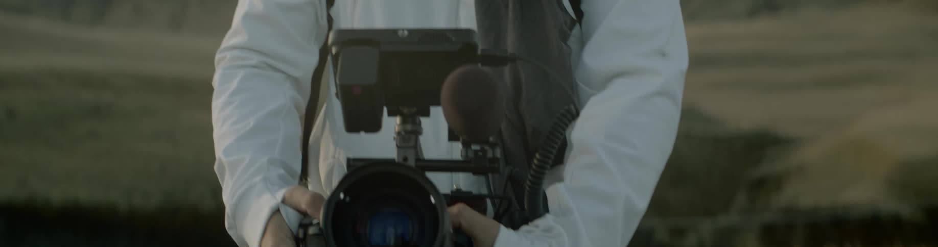 A man adjusts the lens of his camera while standing in an open field