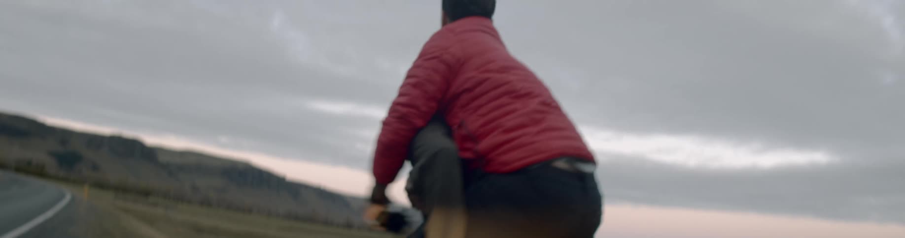 Male holding a camera runs and jumps on a females back as she runs along the side of the road