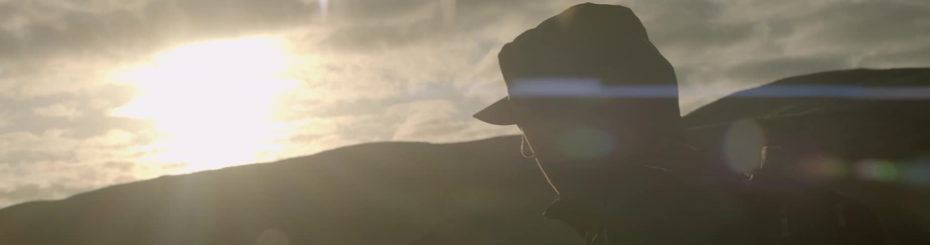 Man wearing a backpack walks across the field at sunset