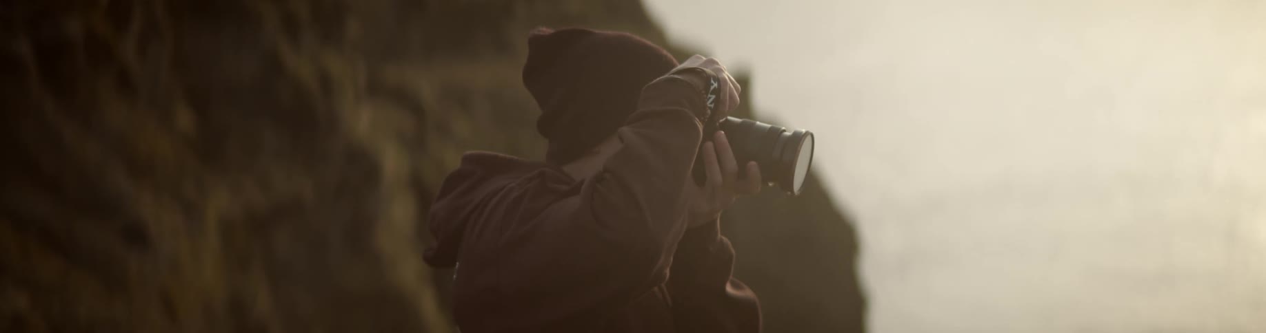 A man standing outside near a cliff takes a photograph then puts the camera down
