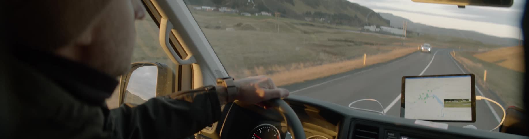 A man sits high up in a drivers seat and travels past cars on a rural road