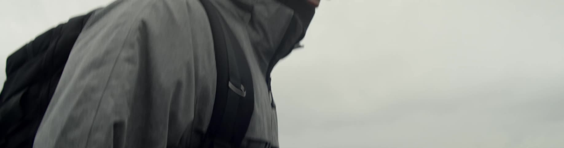Man wearing a backpack and coat walks on the black sand on a cloudy
