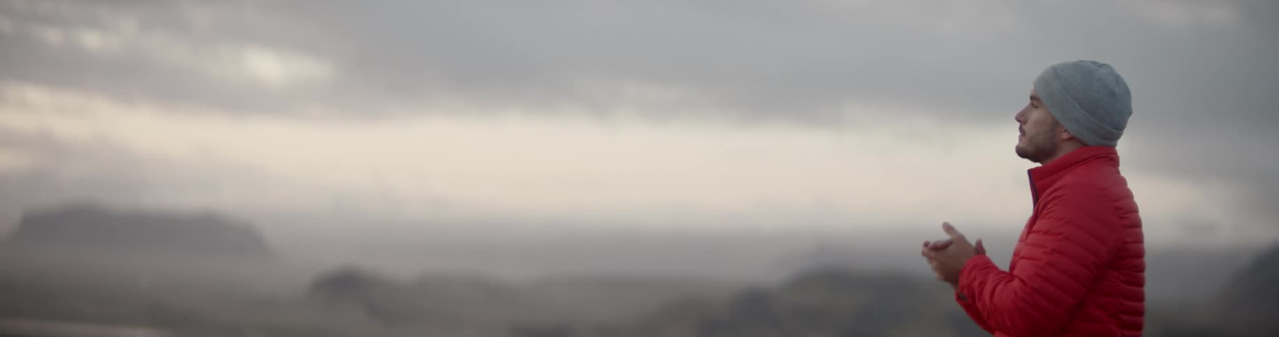 A man stands outside and blows in to his hands while looking across the land