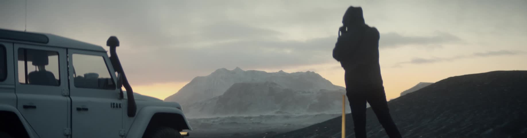 A man stands beside a vehicle looking towards the mountain scenery