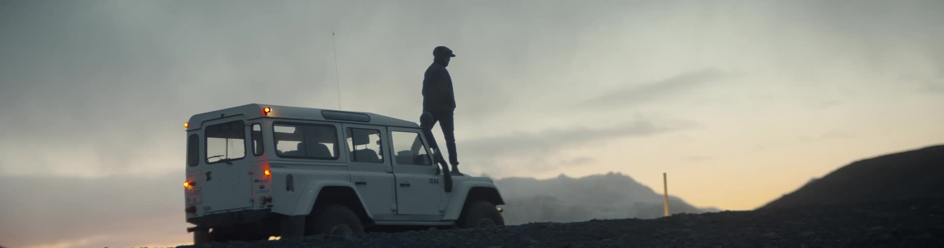 A man is standing on top of a truck at sunset