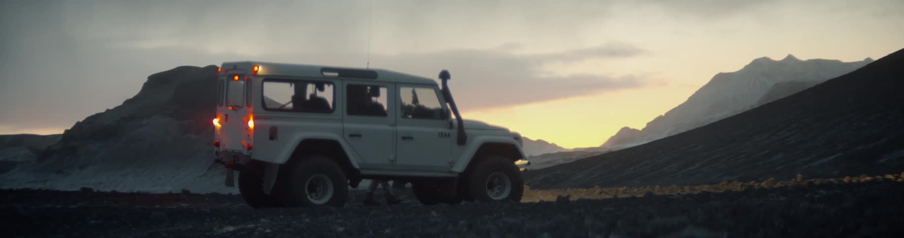 A white suv with all terrain tires is parked at the base of a hill at sunset