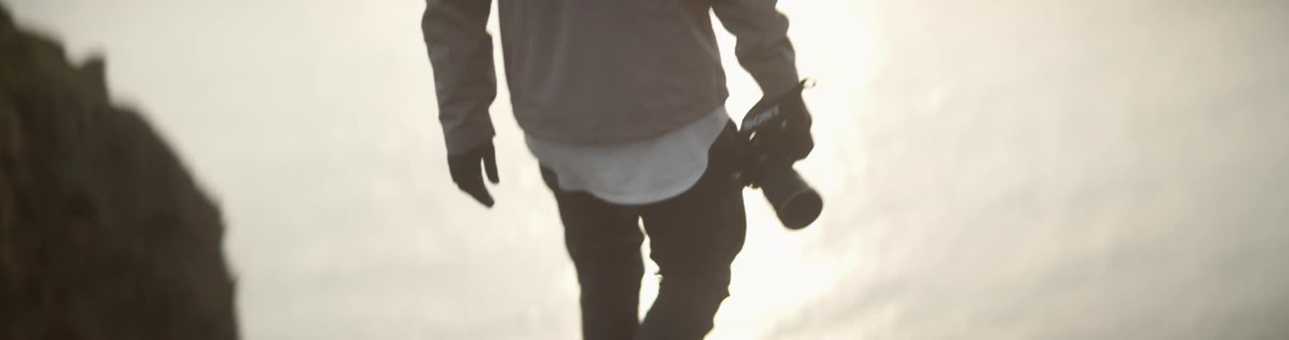 A person walking on a cliff close to the coast holding a camera