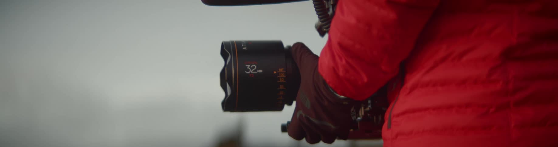 A man in winter coat and gloves adjusts the focus on a professional camera with microphone