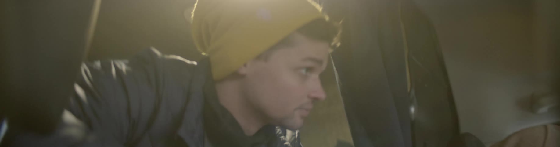 A man wearing a hat leans into the front seat of a vehicle