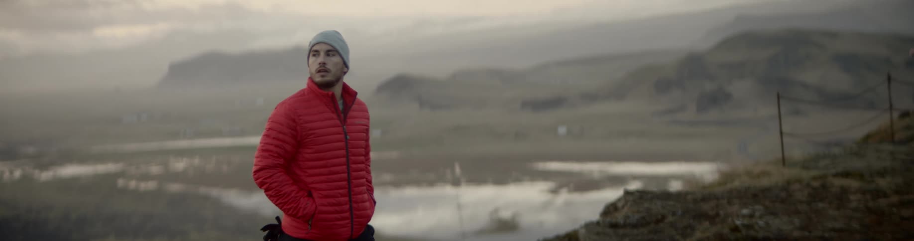 A man in cold weather apparel walks to the top of a hill overlooking a coastal area
