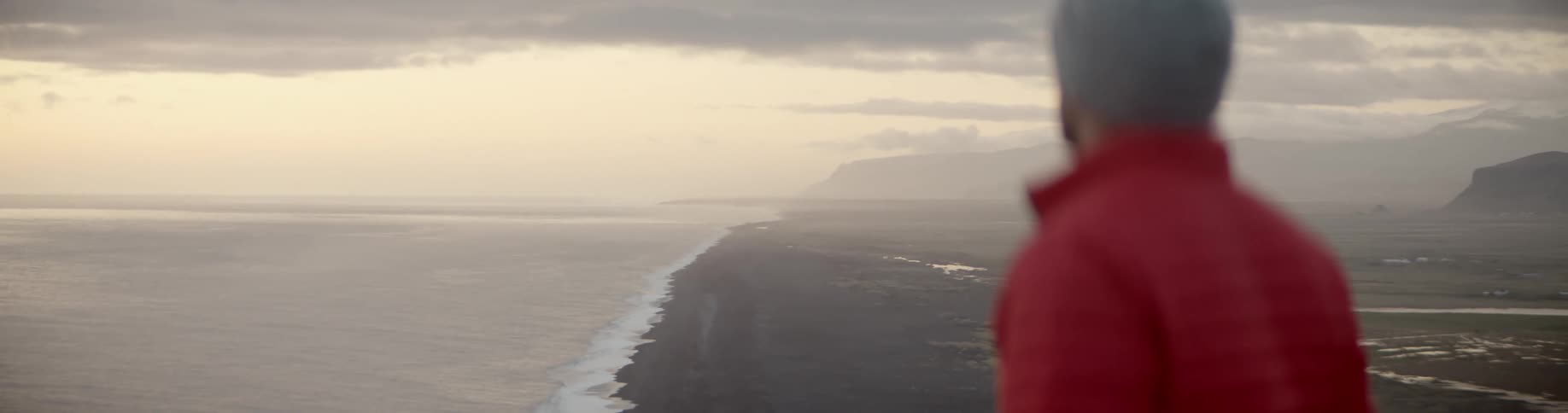Man stands gazing over ocean and mountains in the landscape