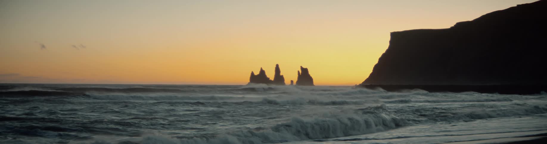 Sea waves crash against the shore at dusk