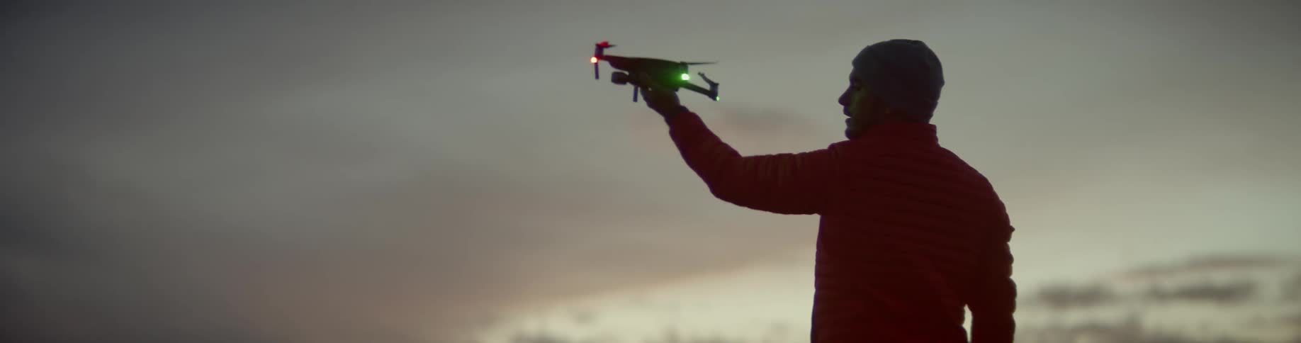 A man holds up a drone while standing on a cliff