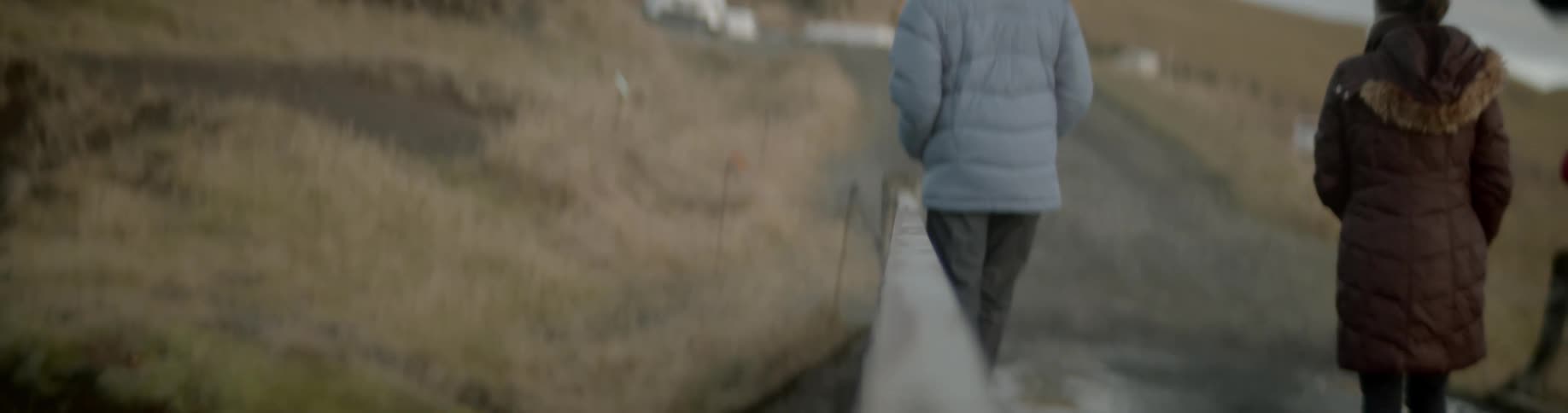 A man looks down over the railing as he and others walk on rural road bridge