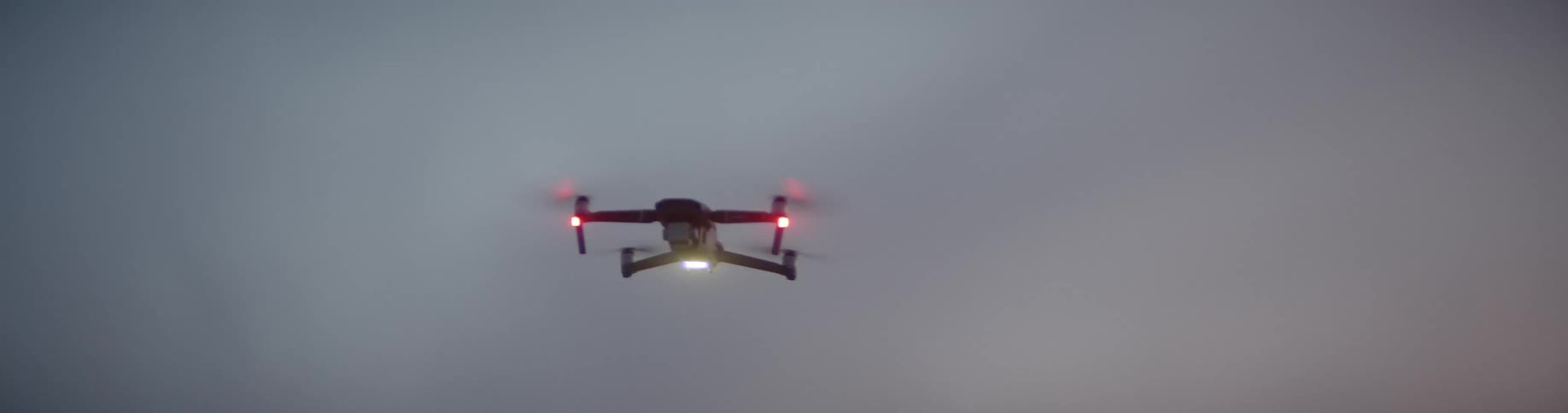 A small drone helicopter with a very bright light on its underside flies overhead