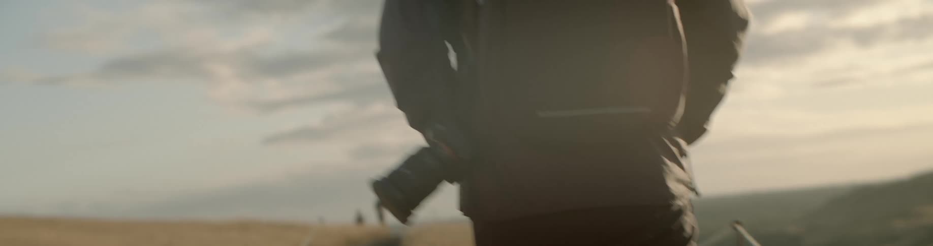 A man carrying a camera walks across a field