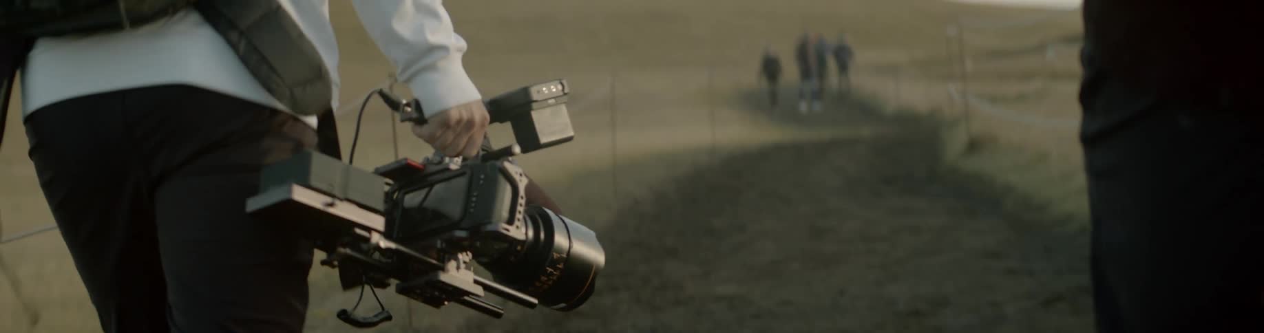Two men walk along a trail while carrying very sophisticated cameras and photography equipment