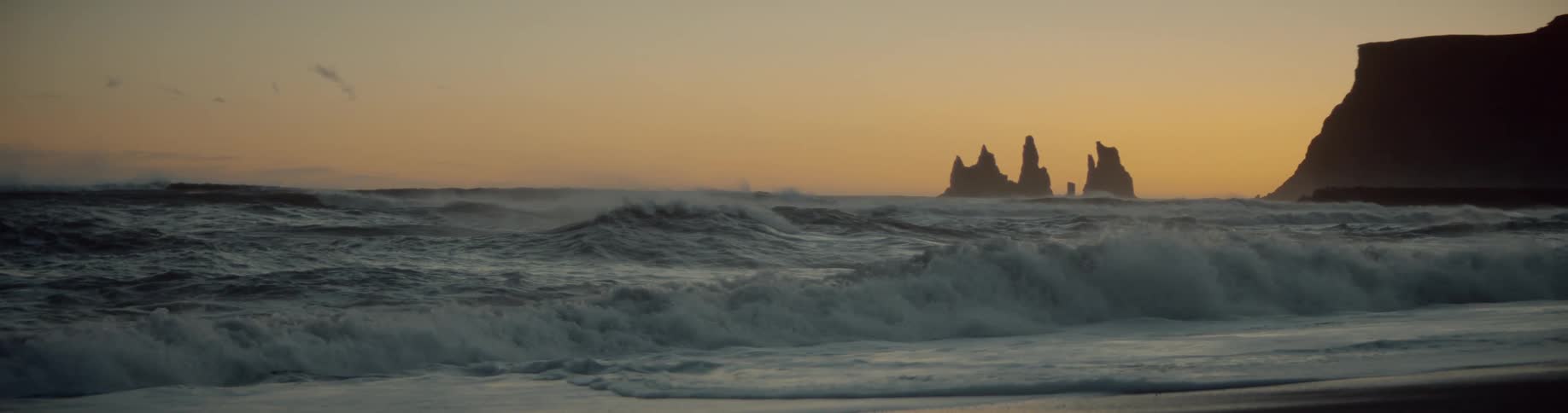Waves crash onto a beach at sunset