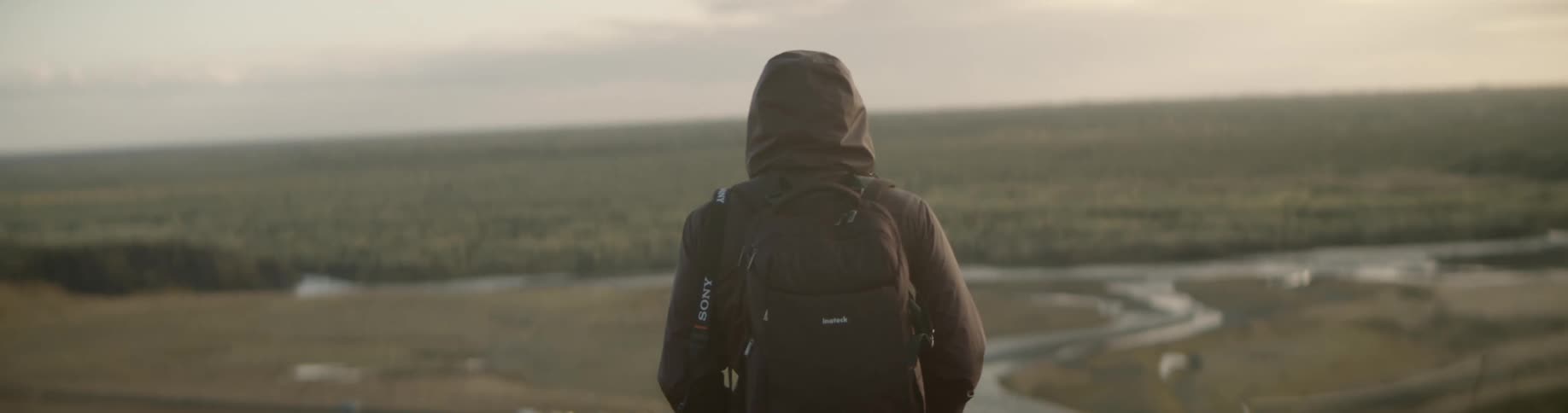 Man wearing a coat and backpack walks across the field