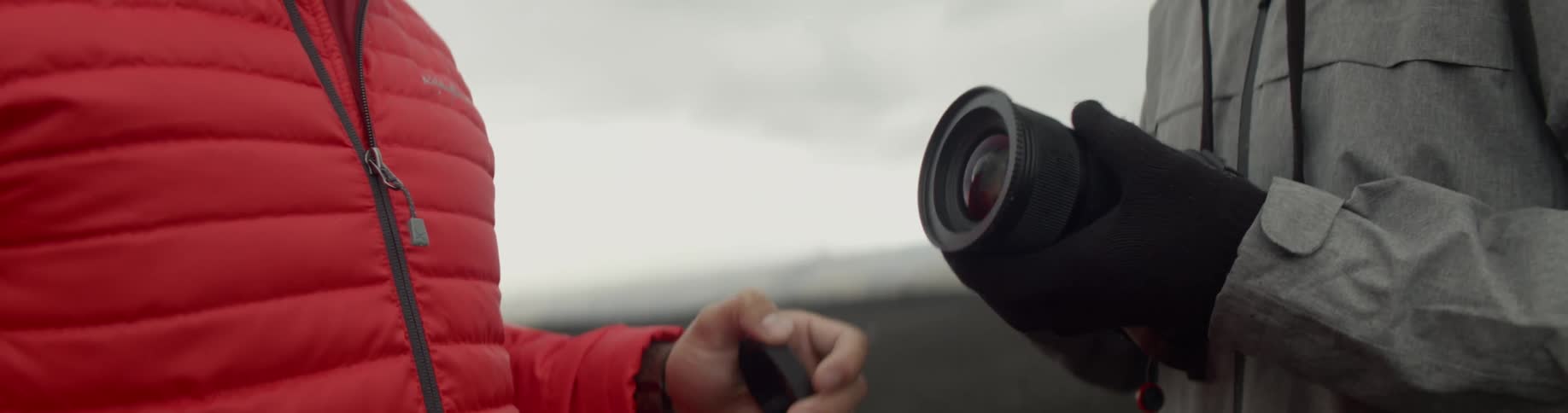 Two people standing outdoors discuss the use of an advanced camera lens