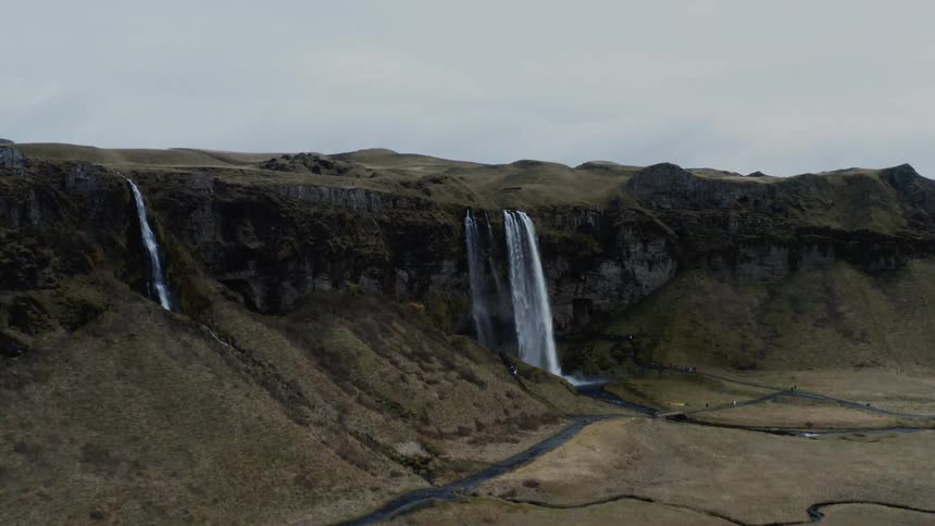 A waterfall crashes in to a river at the bottom of a hill