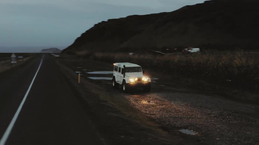 A jeep sits parked next to road near crop fields and mountains