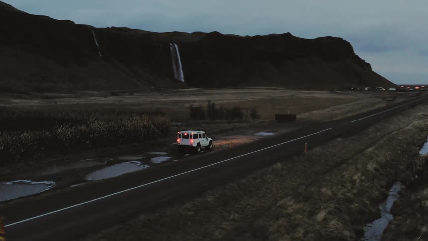All terrain vehicle parked at the side of a country road near mountain with waterfall