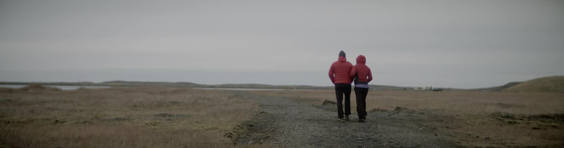 Couple walking on a field towards a lake on a cloudy day