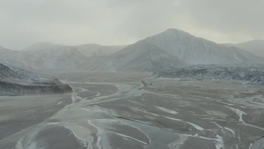 Snow covered mountains and land sit under a cloudy sky