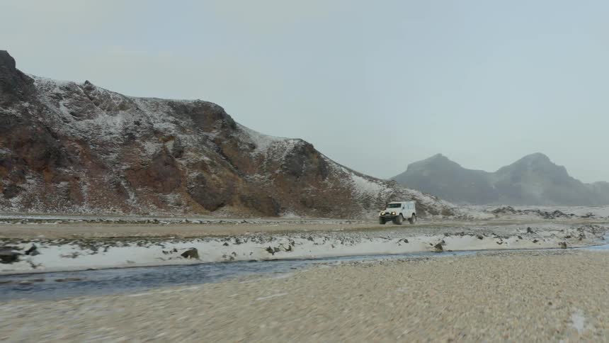 A rugged jeep drives along a dirt road in a remote along the base of snow dusted hills