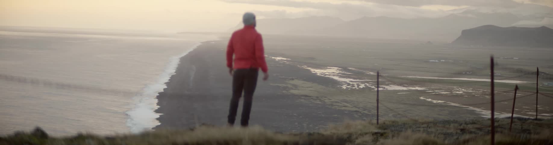 A man stands at the top of a hill and looks at the land