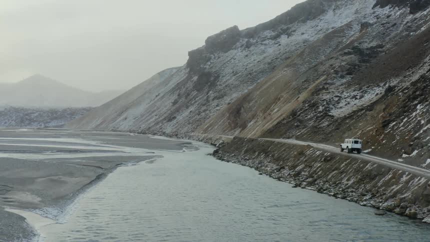 White jeep driving on a narrow road along a lake near the cliffs