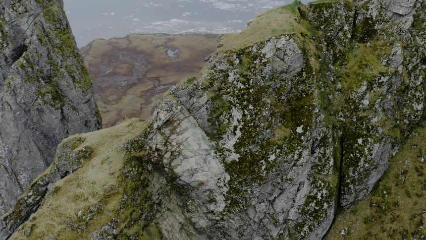 Birds fly above jagged rocky ridge along the coast