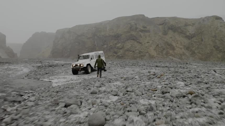 A man walks across a rocky landscape to his vehicle as the snow falls